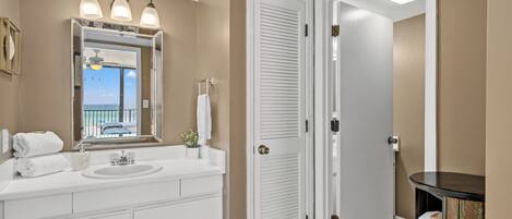 A bathroom with a white vanity, a large mirror, and a view of the ocean through the door.