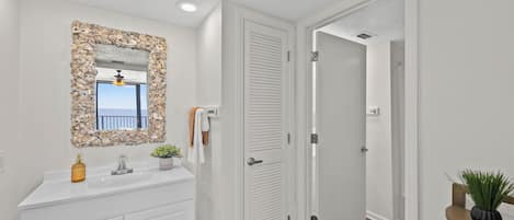 A bathroom with a stone-framed mirror, a white vanity, and a door leading to another room.