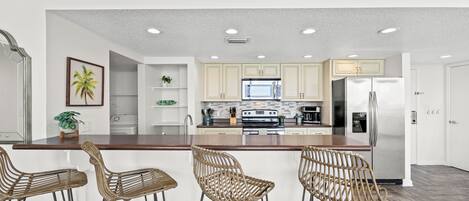 A modern kitchen with a central island, bar stools, and a microwave.