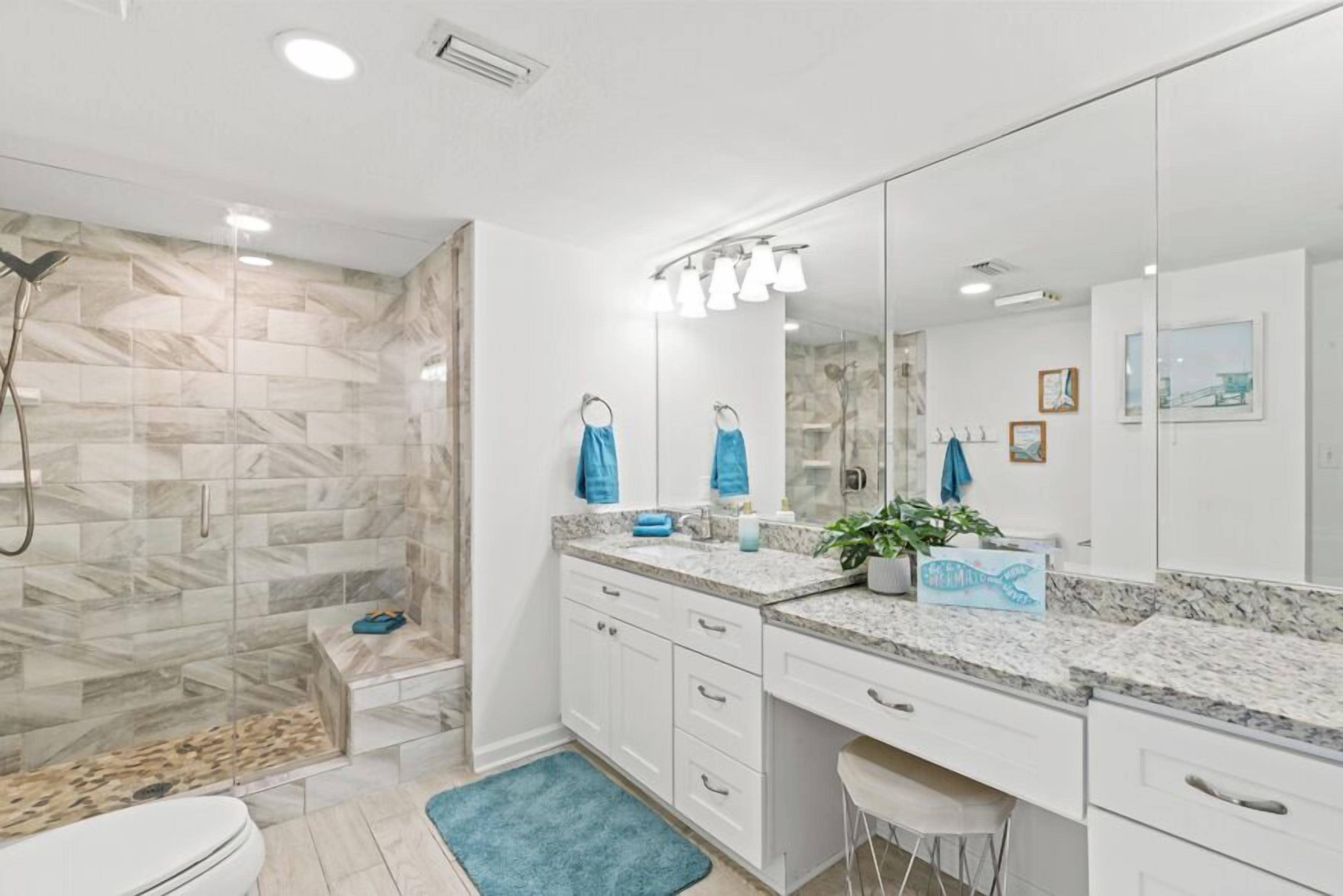 Un baño moderno con cabina de ducha de vidrio, muebles blancos y un espejo grande.