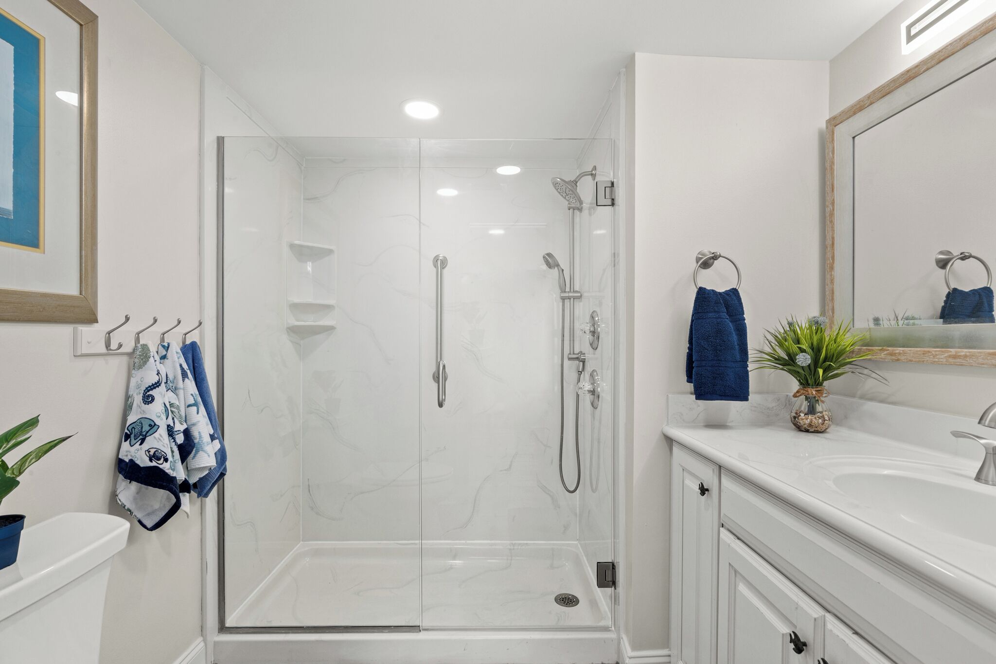 A modern bathroom with a glass-enclosed shower, white marble walls, a large mirror, and a white vanity with a sink.