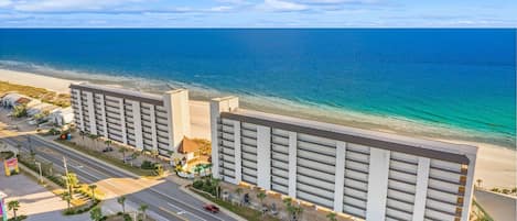 Un hotel frente a la playa con estacionamiento de varios pisos y un área de piscina.