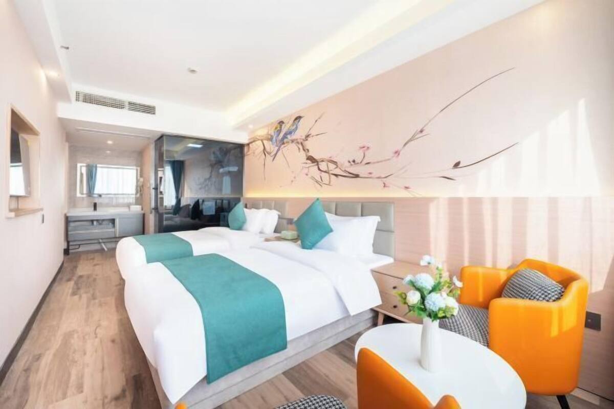 A modern hotel room with a large bed, a desk, and a seating area with orange chairs.