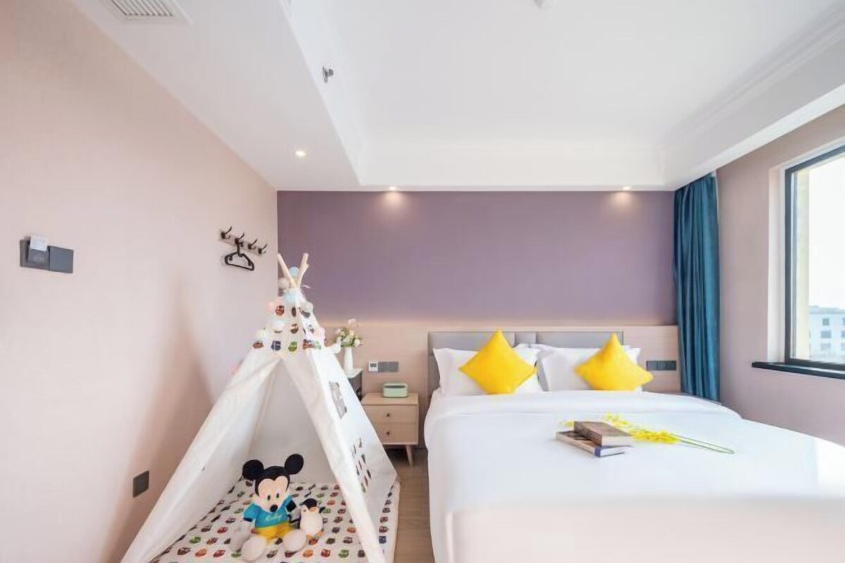 A hotel room with a bed, a Mickey Mouse tent, a nightstand, and a window with curtains.