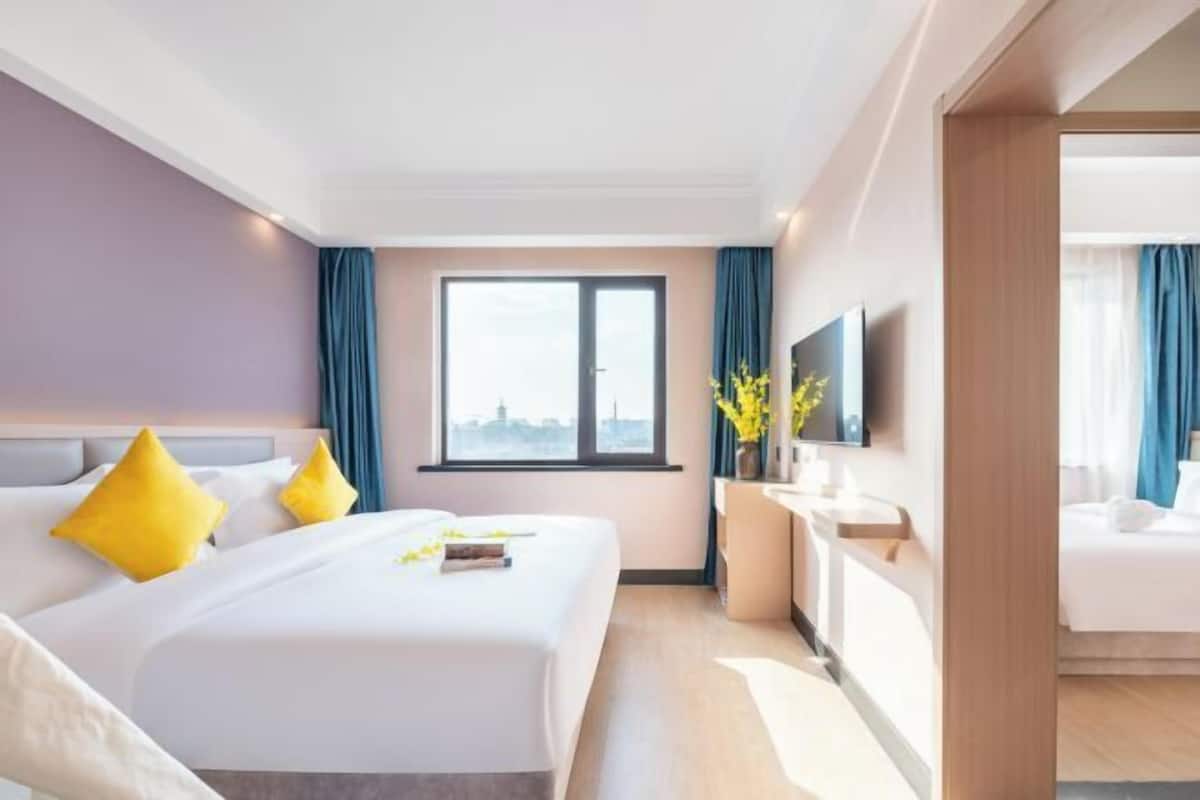 A hotel room with a large bed, a desk, a TV, and a window with curtains.