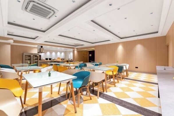 Un comedor moderno con varias mesas y sillas, suelo a cuadros y una cocina al fondo.