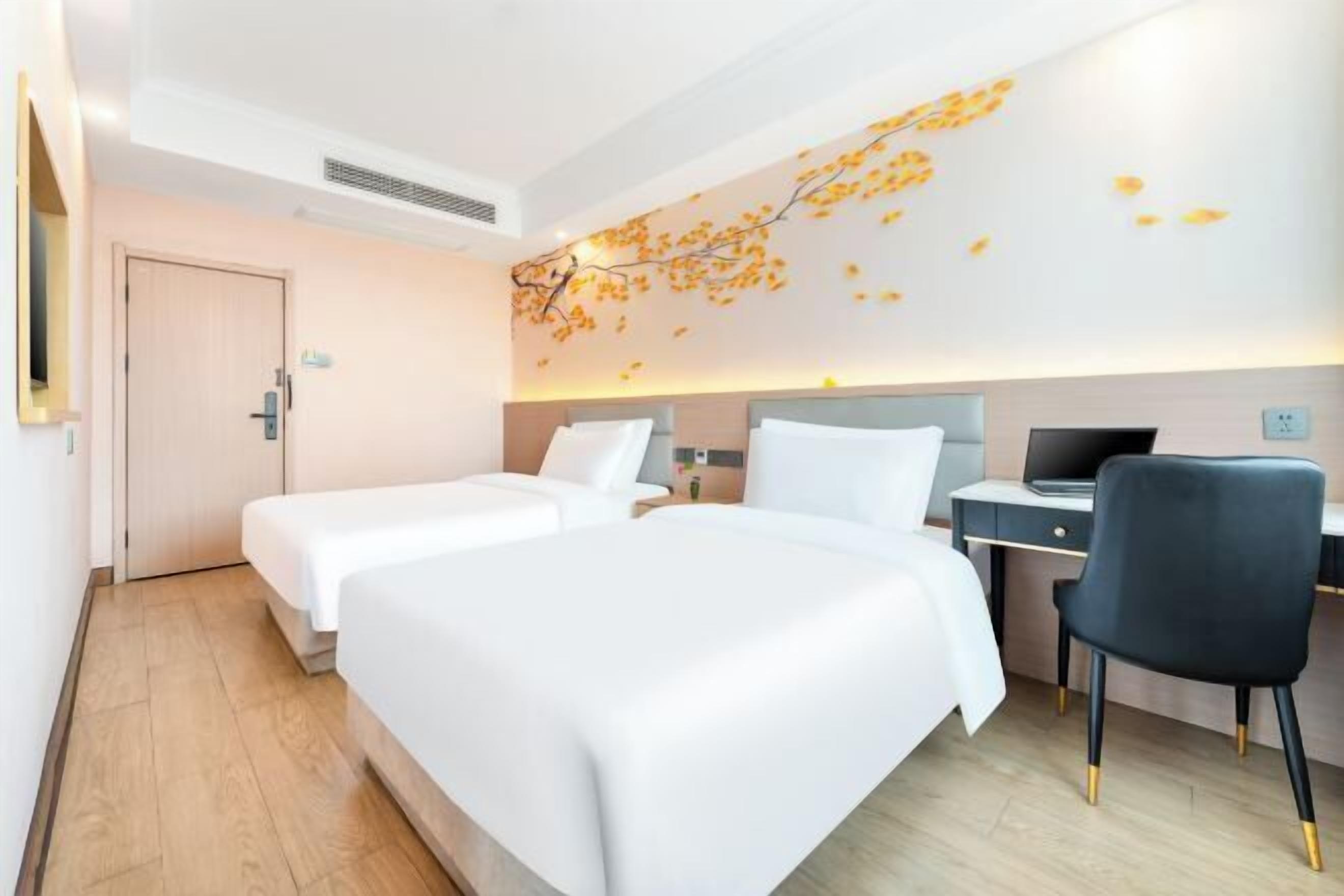 A hotel room with two beds, a desk, a chair, and a wall-mounted TV.