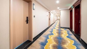 Ein Hotelgang mit Holztüren, einem Teppich mit wellenförmigem Muster und einer Decke mit eingelassenen Leuchten.