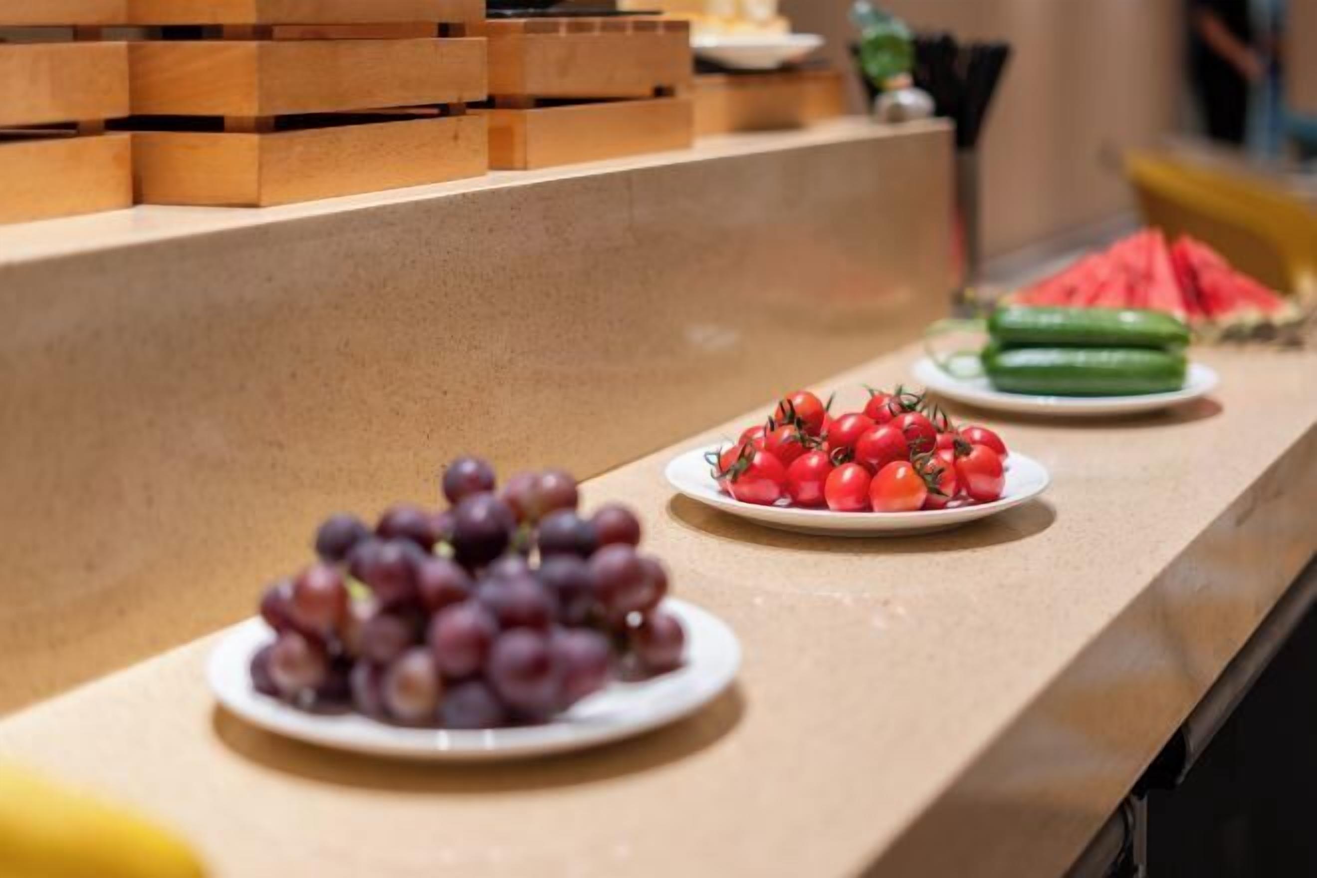 Una barra con platos de uvas y tomates, y una sandía al fondo.