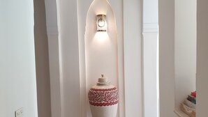 A hallway with white walls, a large decorative vase, and a patterned rug.