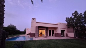 A modern house with a swimming pool, a patio, and a large open door leading to a living area.