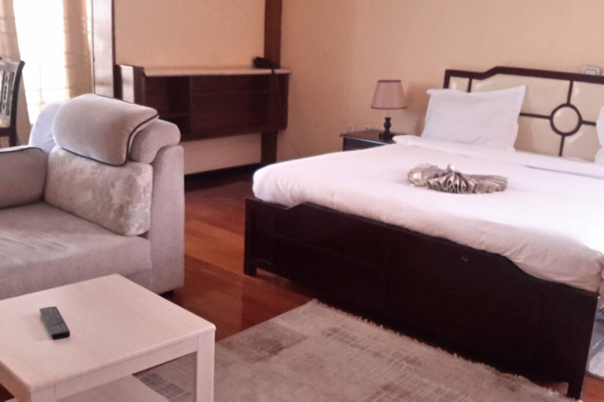 A bedroom with a bed, a sofa, a nightstand, and a small table.
