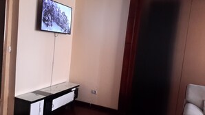 Una habitación con televisor montado en la pared, una puerta de madera y una silla blanca.