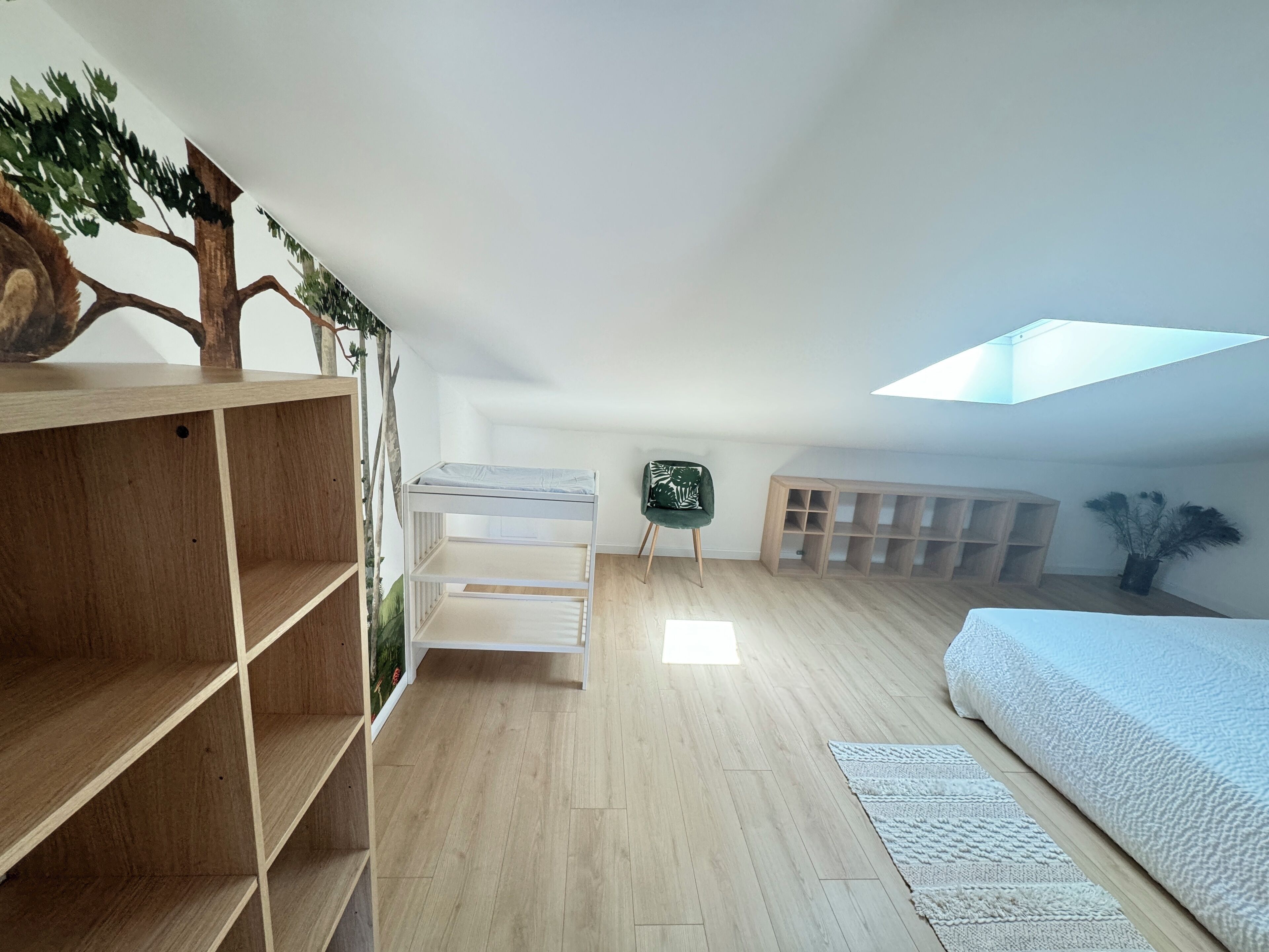 Un amplio dormitorio en el ático con tragaluces, estanterías de madera, una silla verde y un banco empotrado.