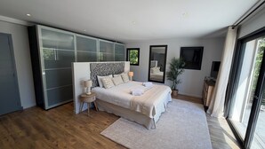 A modern bedroom with a large bed, a nightstand, a mirror, and a potted plant. - Villa Saint-paul-de-vence With Swimming Pool (Saint-Paul-de-Vence)