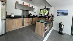 A modern kitchen with wooden cabinets, a stainless steel refrigerator, a built-in oven, a large island with a sink, and a window providing natural light. - Villa Saint-paul-de-vence With Swimming Pool (Saint-Paul-de-Vence)