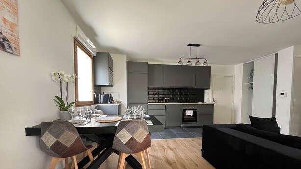 A modern kitchen with grey cabinets, a built-in oven, and a dining area with a black table and chairs.