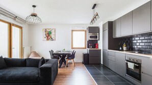 A modern kitchen with dark tiles, stainless steel appliances, and a dining area with a black sofa and wooden flooring.
