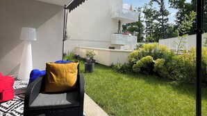 A covered outdoor seating area with a black wicker sofa, a yellow cushion, and a patterned rug.