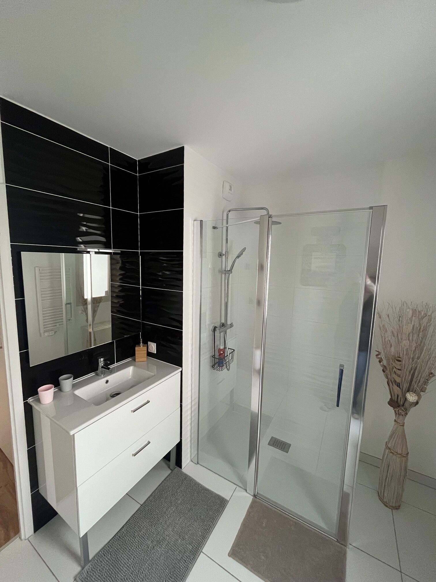 A modern bathroom with a glass shower enclosure, a white vanity with a mirror, and black tiled walls.