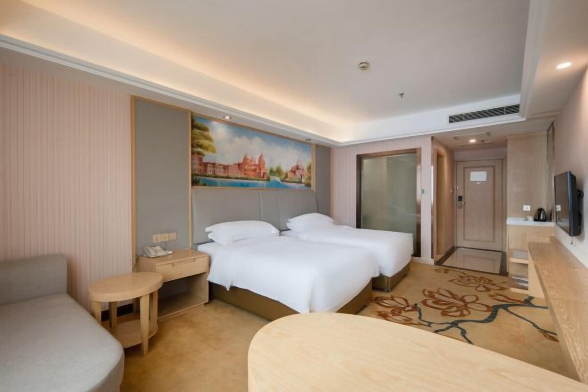 A hotel room with two beds, a desk, a chair, a TV, and a painting on the wall.
