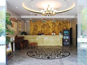 En hotellobby med ett marmorgolv, en receptionsdisk, en kristallkrona och en vägg med en dekorativ relief.