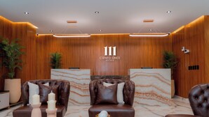 A modern lobby with wooden paneling, two leather sofas, a glass coffee table, and a marble accent wall. - Hotels 111 (San Andrés)