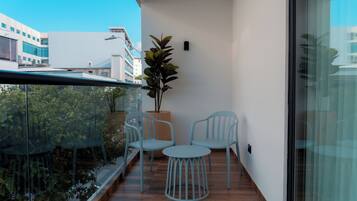 Uma varanda com duas cadeiras azul-claras e uma pequena mesa redonda, um vaso com planta e vista para edifícios ao fundo.