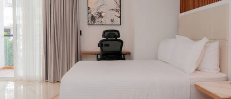 A hotel room with a large bed, a desk with a chair, a window with curtains, and a wall-mounted artwork.