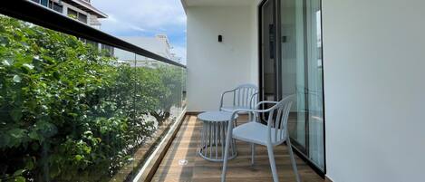 Een balkon met een houten vloer, twee witte stoelen en een glazen deur naar een kamer.