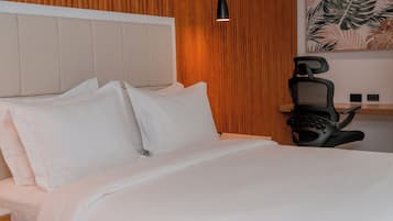 Una cama bien tendida con sábanas blancas, cabecera de madera y una silla negra con auriculares.