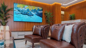A modern lobby with leather sofas, a large flat-screen TV, wooden paneling, and potted plants. - Hotels 111 (San Andrés)