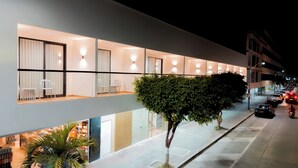 A modern hotel with a row of rooms, a covered outdoor seating area, and a tree-lined street. - Hotels 111 (San Andrés)