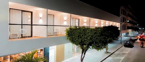 A modern hotel with a row of rooms, a covered outdoor seating area, and a tree-lined street.