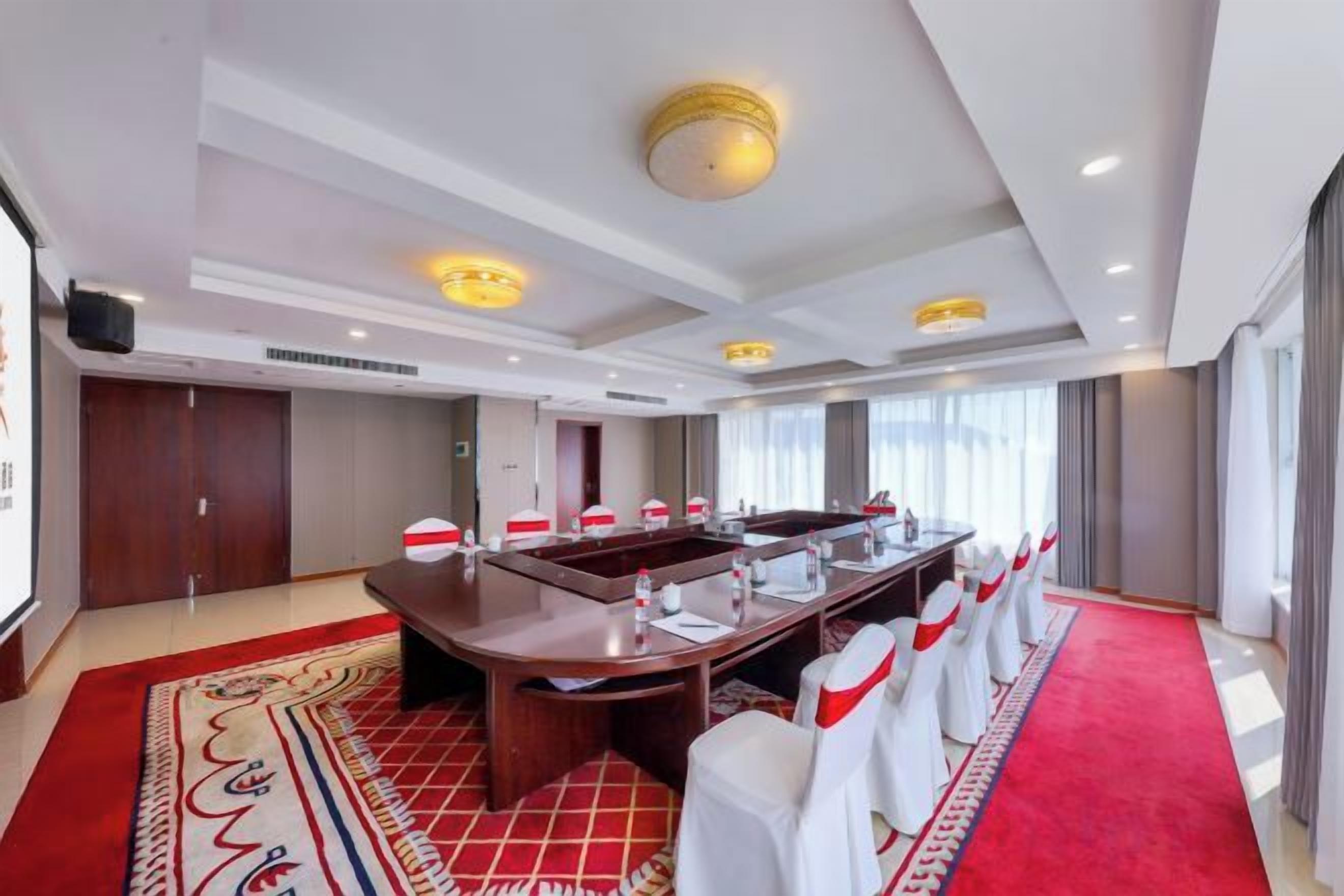 A conference room with a long table, white chairs, a red carpet, and a large window.