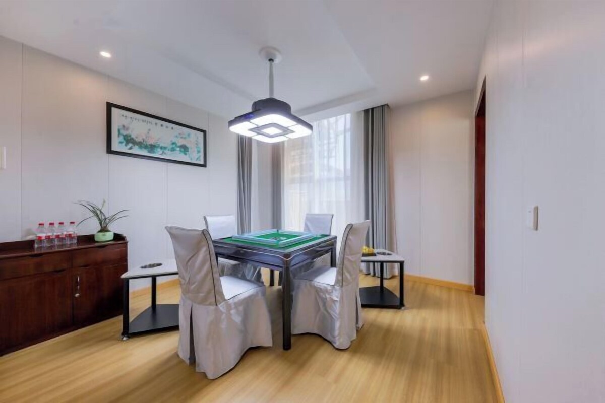 A modern hotel room with a wooden floor, a dining table with chairs, a ceiling light, and a framed artwork on the wall.