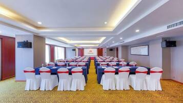 Un salón de conferencias con filas de mesas y sillas, suelo alfombrado e iluminación empotrada en el techo.