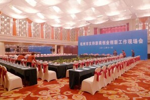 A banquet hall with tables set for a formal event, a stage with a blue backdrop, and a carpeted floor. - Hangzhou Fuyang Yaoyue International Hotel (Enbo Avenue) (Hangzhou)