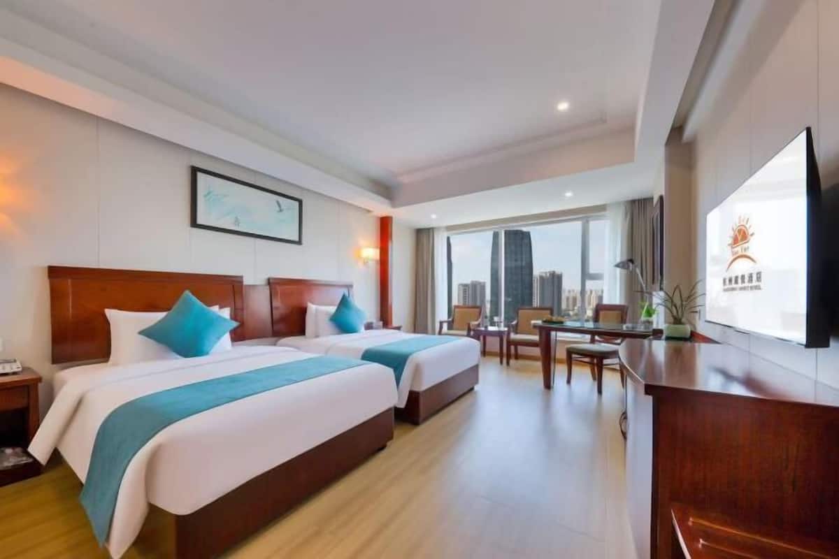 A hotel room with two beds, a desk, and a large TV.