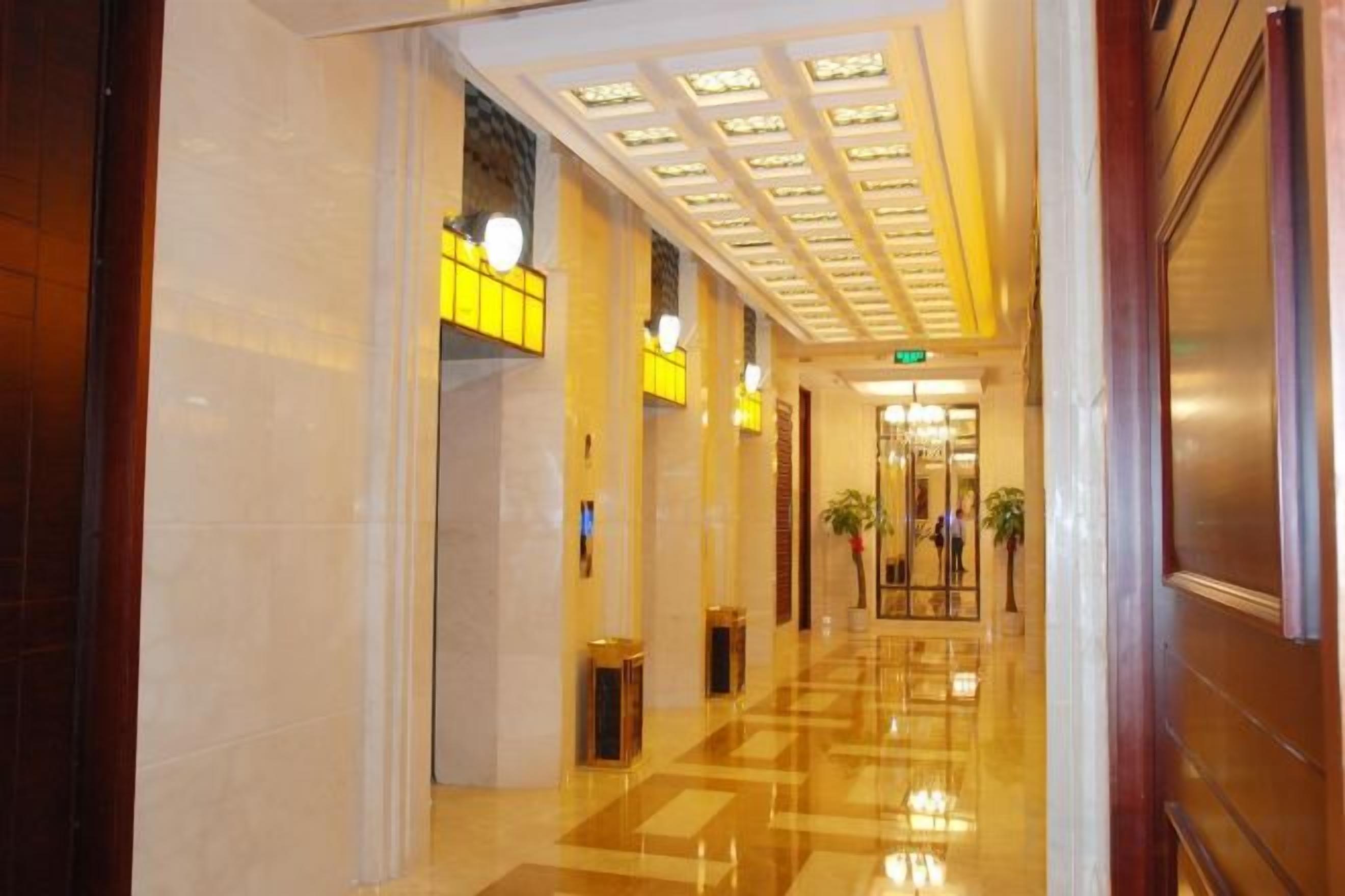 A hotel corridor with a polished floor, a ceiling with recessed lighting, and a door on the right.