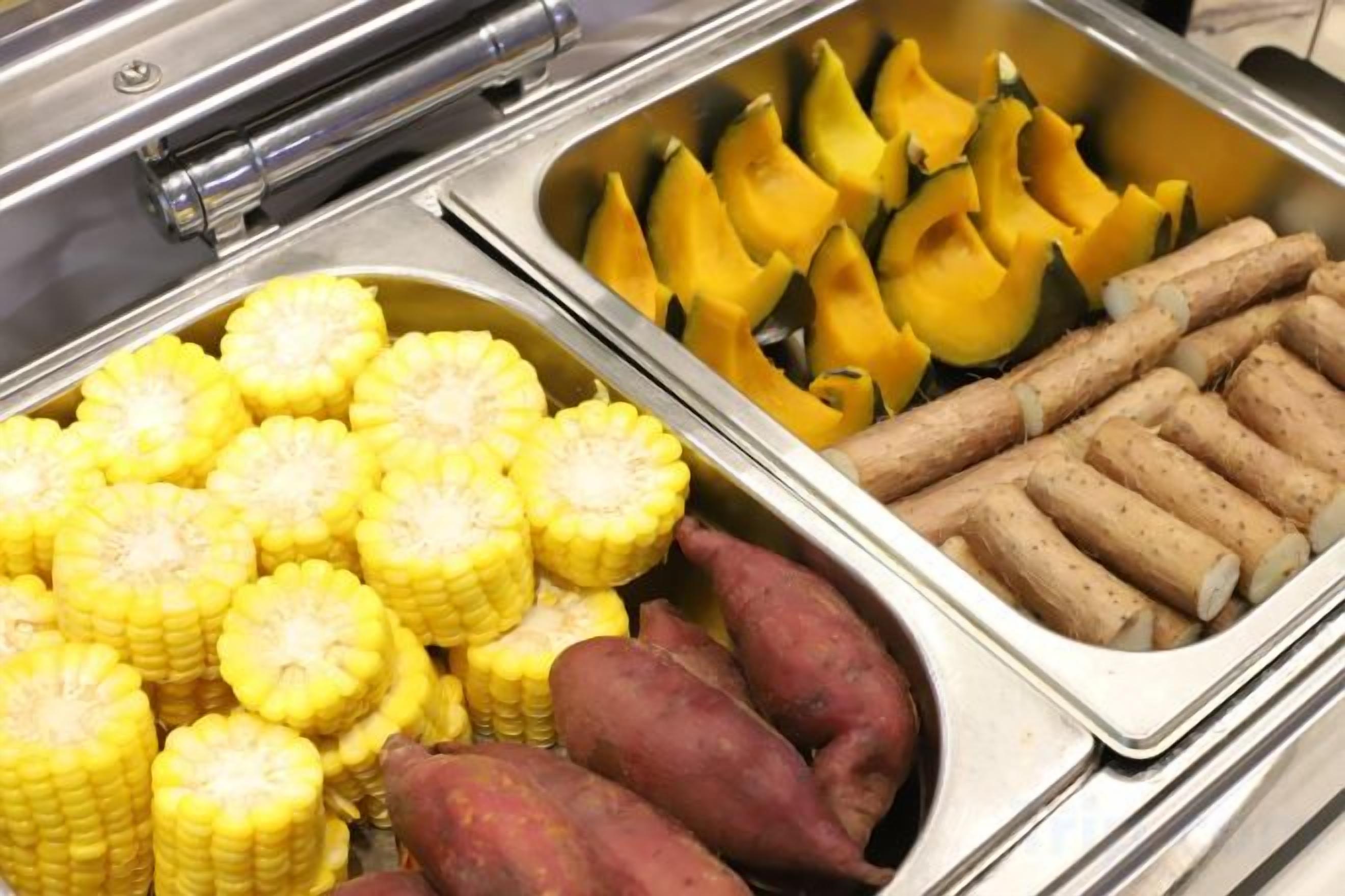 Un bufé con mazorcas de maíz, batatas y calabacín amarillo.