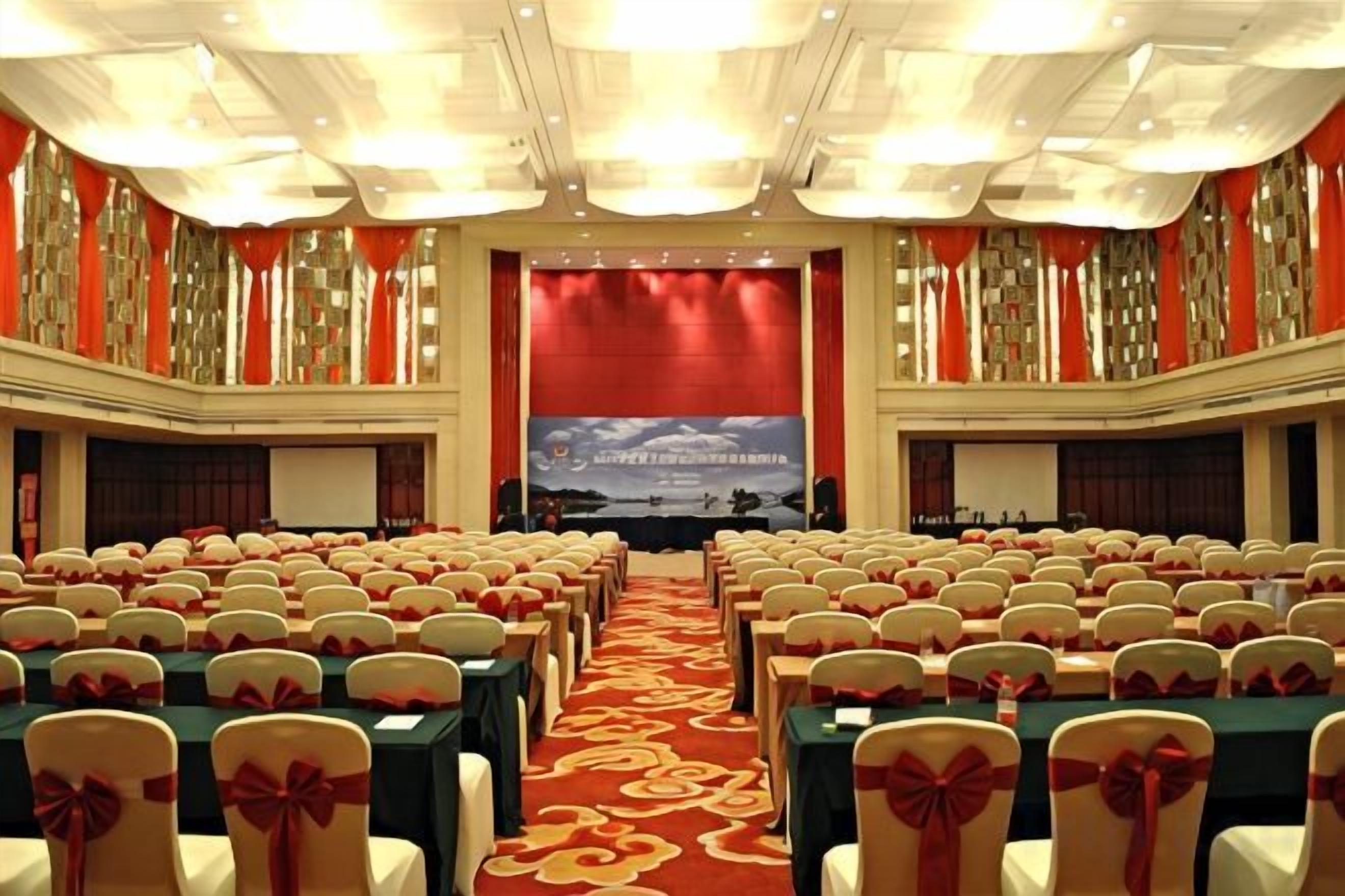 Una sala conferenze con file di tavoli e sedie, un palco e uno striscione.