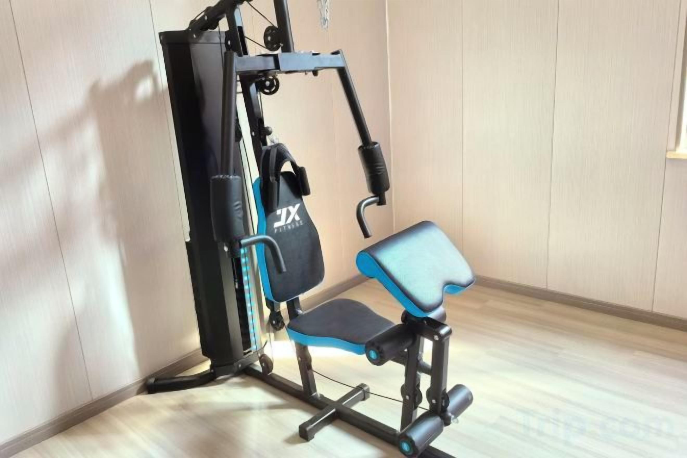 Un gimnasio con una máquina de ejercicios azul y negra, un estante fijado a la pared y suelo de madera.