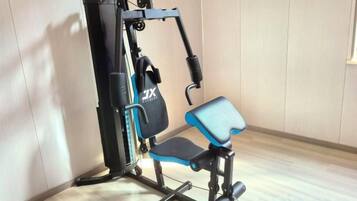 Un gimnasio con una máquina de ejercicios azul y negra, un estante fijado a la pared y suelo de madera.