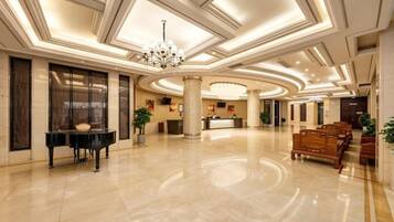 A spacious lobby with a grand piano, a reception desk, and seating areas.