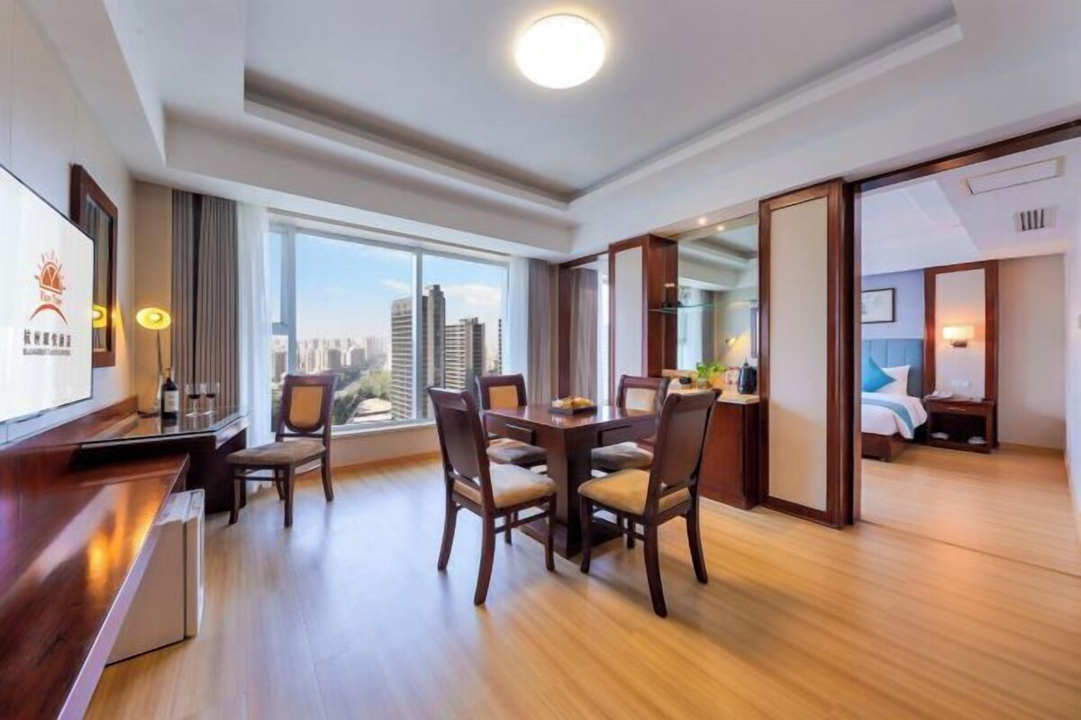 A hotel room with a dining area, a large window with a city view, and a separate bedroom.