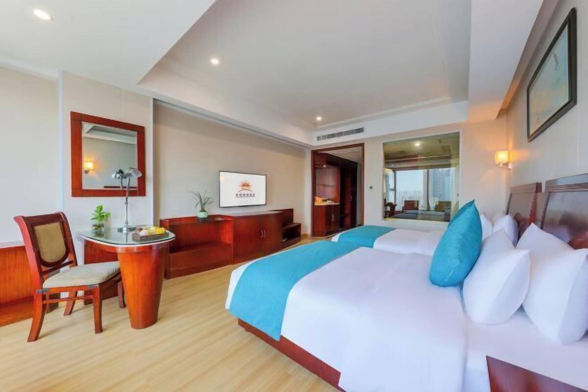 A hotel room with a large bed, a desk with a chair, a mirror, and a view of the city.
