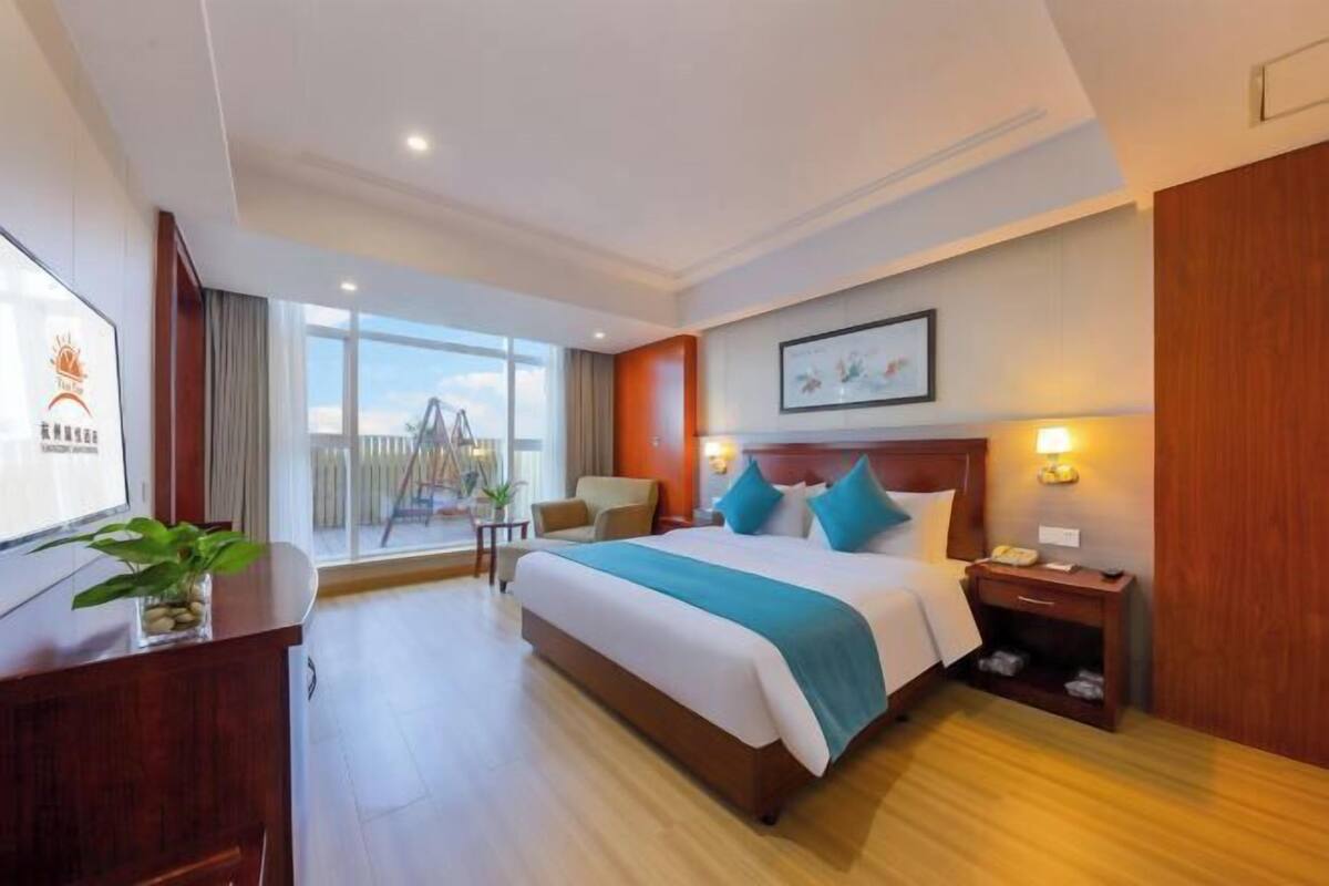 A hotel room with a large bed, a desk, a chair, a TV, and a balcony with a view.