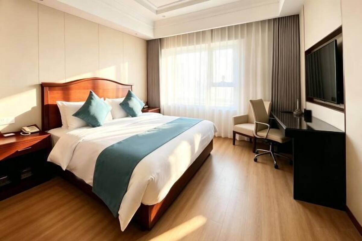 A hotel room with a large bed, a desk with a chair, a television, and a window with curtains.