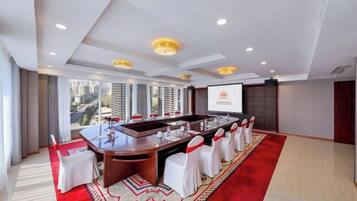 A conference room with a long table, white chairs, and a red carpet.